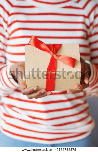 african American woman gives or receives a gift. a\
happy millennial woman with a cardboard box and a red ribbon in her\
hands. an anniversary and birthday gift for a friend or wife. party\
joy and