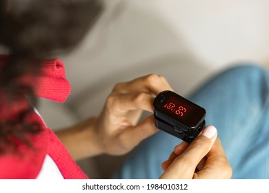 African American Woman Hands Measures  Pulse And Oxygen Saturation Using A Pulse Oximeter Sitting On The Couch At Home, Healthcare Concept