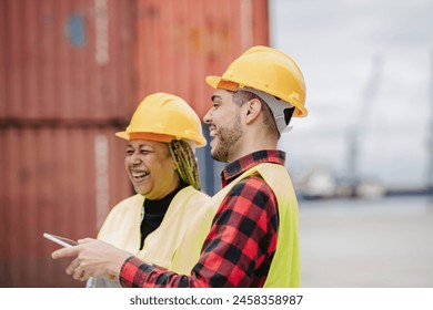 African American woman and Hispanic man in hard hats and safety vests laughing together at an industrial site. - Powered by Shutterstock