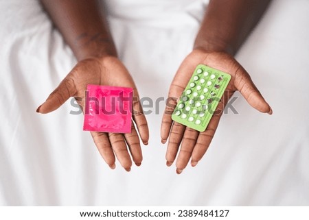 African american woman holding condom and birth control pills at bedroom