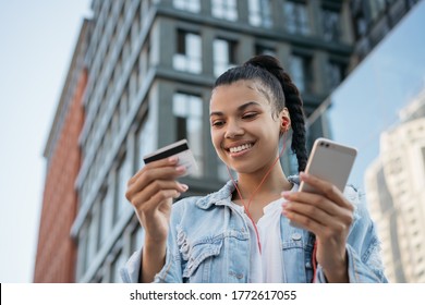 African American woman holding credit card, using smartphone for online shopping, mobile banking. Young freelancer receive payment, check balance. Hipster girl ordering food online, booking tickets - Powered by Shutterstock