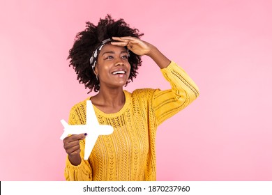 African american woman holding paper plane. Young woman feeling exciting because of traveling. Looking in the distance with her hand on her forehead