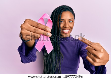 African american woman holding pink cancer ribbon smiling happy pointing with hand and finger 