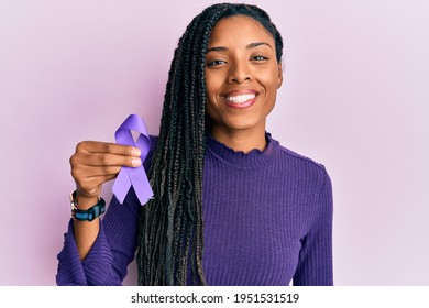 African american woman holding purple ribbon awareness looking positive and happy standing and smiling with a confident smile showing teeth  - Powered by Shutterstock