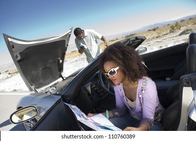 An African American Woman Holding Road Map With Man Checking Car