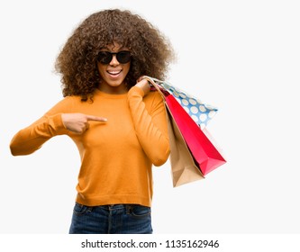 African american woman holding shopping bags with surprise face pointing finger to himself