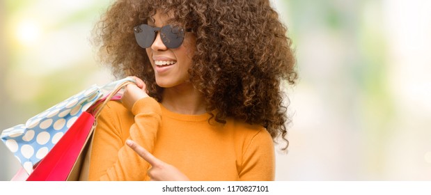 African american woman holding shopping bags very happy pointing with hand and finger