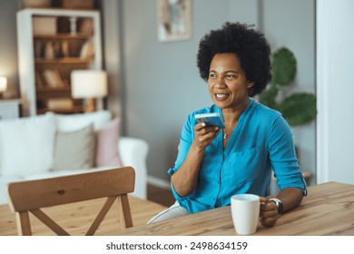 African American woman holding a smartphone near her face, recording voice messages, or having a phone call on speakerphone. Woman using voice assistant on smart phone - Powered by Shutterstock