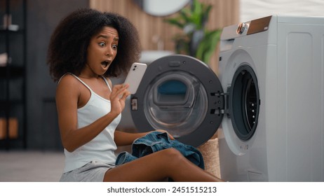 African American woman housewife sad upset shocked biracial ethnic girl pull out of washing machine laundry take jeans find broken wet smartphone forgot mobile phone in cloth pocket waterproof gadget - Powered by Shutterstock