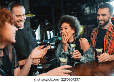 African american woman laughing near friends with tequila shots in bar - Powered by Shutterstock