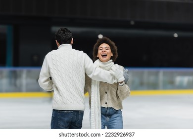 African american woman laughing while ice skating with boyfriend on ice rink  - Shutterstock ID 2232926937