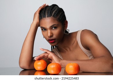 African American Woman With Long Dark Braids And Orange Fruits Poses Indoor.