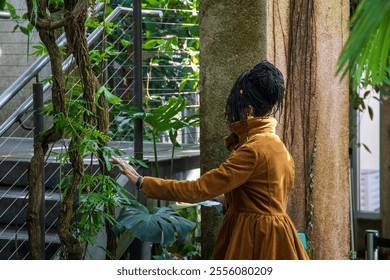 An African American woman with long sisterlocks wearing a brown coat and sunglasses surrounded by lush green trees and plants at Atlanta Botanical Garden in Atlanta Georgia USA - Powered by Shutterstock