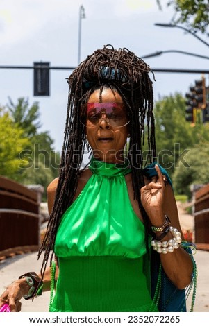 An African American woman with long sisterlocks wearing a green top, a pearl bracelet, sunglasses on a bridge surrounded by lush green trees at the University of Georgia in Athens Georgia USA