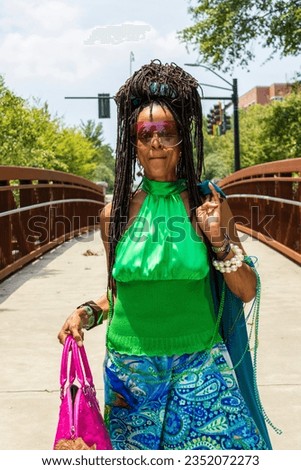 An African American woman with long sisterlocks wearing a green top, blue skirt carrying a pink purse on a bridge with lush green trees at the University of Georgia in Athens Georgia USA