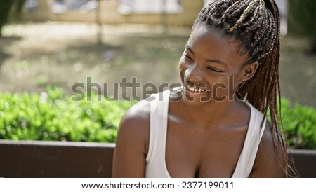 African american woman looking to the side sitting on bench smiling at park