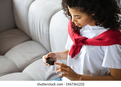 African American woman measures  pulse and oxygen saturation using a pulse oximeter sitting on the couch at home, healthcare concept