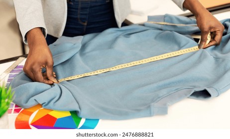 African American woman measuring a shirt using a tape measure. The individual is carefully extending the tape measure along the length and width of the cloth to determine its dimensions accurately. - Powered by Shutterstock