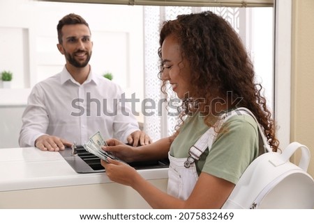 African American woman with money at cash department window in bank. Currency exchange