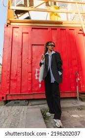 African American Woman In Oversize Suit And Sunglasses Listening Music On Urban Street In Prague