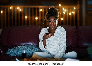 african american woman in pajamas staying up late at night eating pizza and watching tv