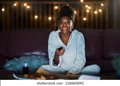 African American Woman In Pajamas Staying Up Late At Night Eating Pizza And Watching Tv