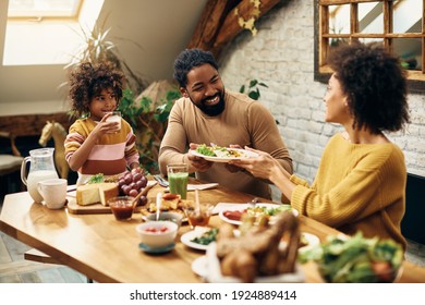 African American woman passing food to her husband during family meal in dining room. Focus is on man. - Powered by Shutterstock