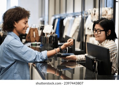 African american woman paying for her purchases with smartwatch, asian cashier receiving payment - Powered by Shutterstock