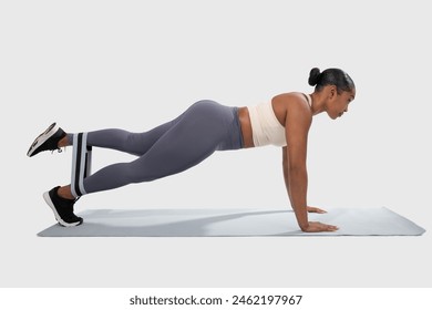 African American woman is performing push-ups on a mat in a gym or a fitness studio. She is engaging her upper body muscles while maintaining a plank position, using resistance band - Powered by Shutterstock