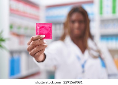 African american woman pharmacist smiling confident holding condom at pharmacy