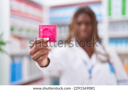 African american woman pharmacist smiling confident holding condom at pharmacy