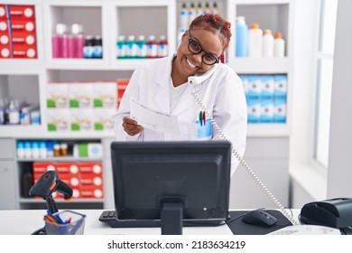 African american woman pharmacist talking on telephone reading prescription at pharmacy - Powered by Shutterstock