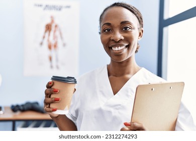 African american woman physiotherapist holding medical report drinking coffee at rehab clinic - Powered by Shutterstock