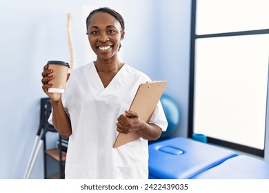 African american woman physiotherapist holding medical report drinking coffee at rehab clinic - Powered by Shutterstock