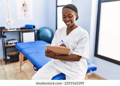 African american woman physiotherapist smiling confident writing medical report at rehab clinic - Powered by Shutterstock