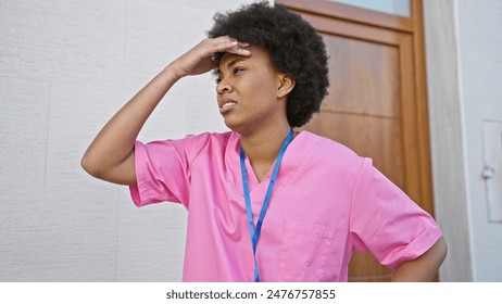 African american woman in pink scrubs looking stressed while standing outside a hospital. - Powered by Shutterstock