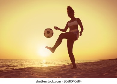 African American woman playing football on beach at sunset