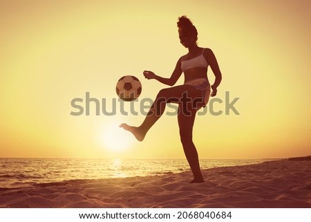 African American woman playing football on beach at sunset