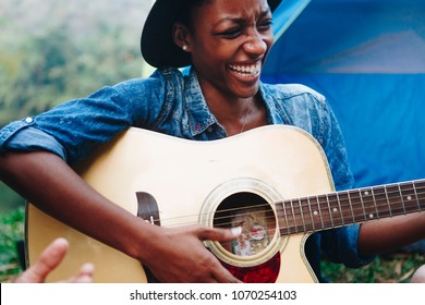 African American Woman Playing A Guitar At A Campsite