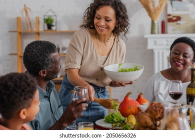 African american woman pouring salad near family and son during thanksgiving celebration - Powered by Shutterstock