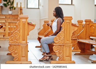 African american woman praying in the church. Believers meditates in the cathedral and spiritual time of prayer. Afro girl hold rosary and sitiing on bench.