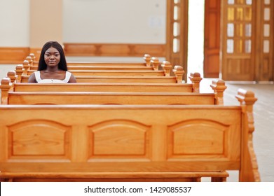 African american woman praying in the church. Believers meditates in the cathedral and spiritual time of prayer. Afro girl sitting on bench.