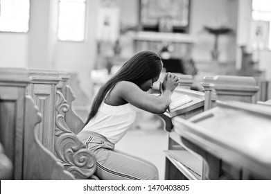 African american woman praying in the church. Believers meditates in the cathedral and spiritual time of prayer. Afro girl folded hands while sitting on bench.