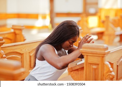 African american woman praying in the church. Believers meditates in the cathedral and spiritual time of prayer. Afro girl folded hands while sitting on bench.