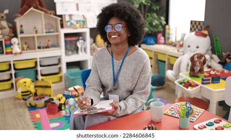 African american woman preschool teacher smiling confident writing on document at kindergarten - Shutterstock ID 2284606845