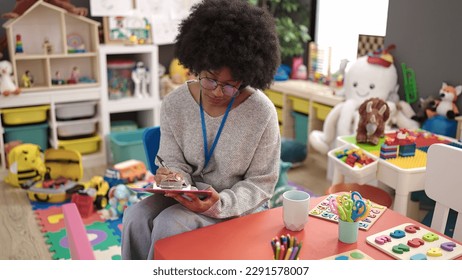 African american woman preschool teacher smiling confident writing on document at kindergarten - Shutterstock ID 2291578007