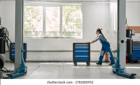 African american woman professional female mechanic pulling, carrying tool box cart in auto repair shop. Car service, maintenance, people concept. Side view. Selective focus. Web Banner - Powered by Shutterstock