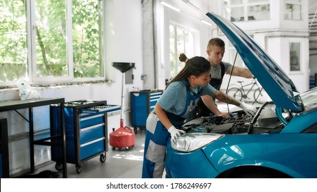 African american woman, professional female mechanic repairing car engine, tighten, screw with spanner while her colleague holding torch under car hood at service station. Side view. Web Banner