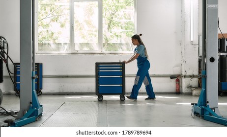 African american woman professional female mechanic pulling, carrying tool box cart in auto repair shop. Car service, maintenance, people concept. Side view. Selective focus. Web Banner - Powered by Shutterstock