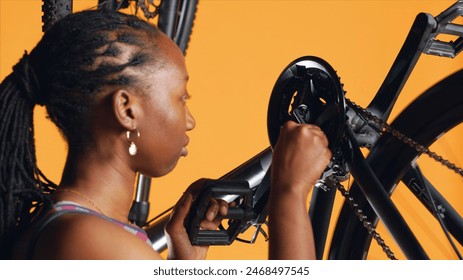 African american woman pushing pedals to spin bike wheel, inspecting it, using screwdriver and hex socket wrench to fix it, close up shot. Riding hobbyist testing bicycle crank arm and chain rings - Powered by Shutterstock